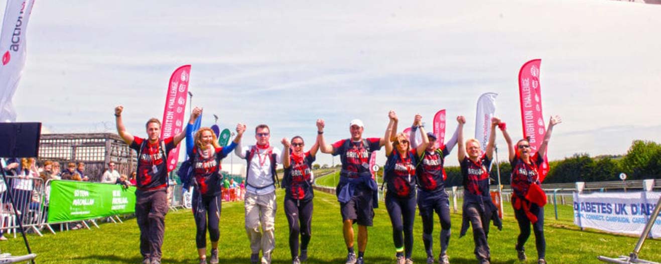 A line of people with their hands in their air and looking happy at the finish line of a charity challenge event.