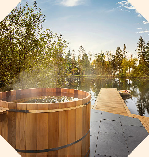 A wooden hot tub alongside a lake with a wooden jetty.