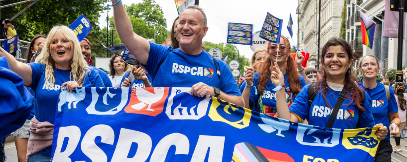 A group of RSPCA representatives at a pride parade waving flags and holding a banner.