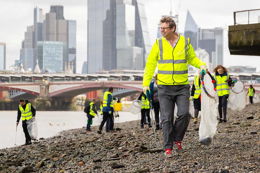 A group of people in high vis jackets carrying out a beach clean on a shingle beach.