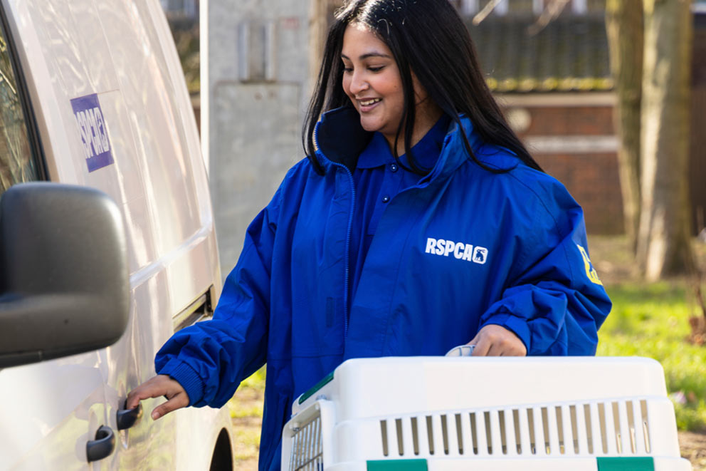 An RSPCA animal rescue volunteer opens a van while carrying a pet carrier.