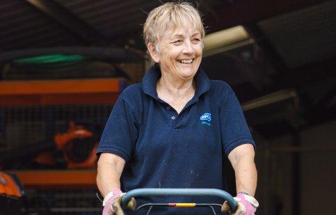 A female volunteer standing behind a lawn mower.