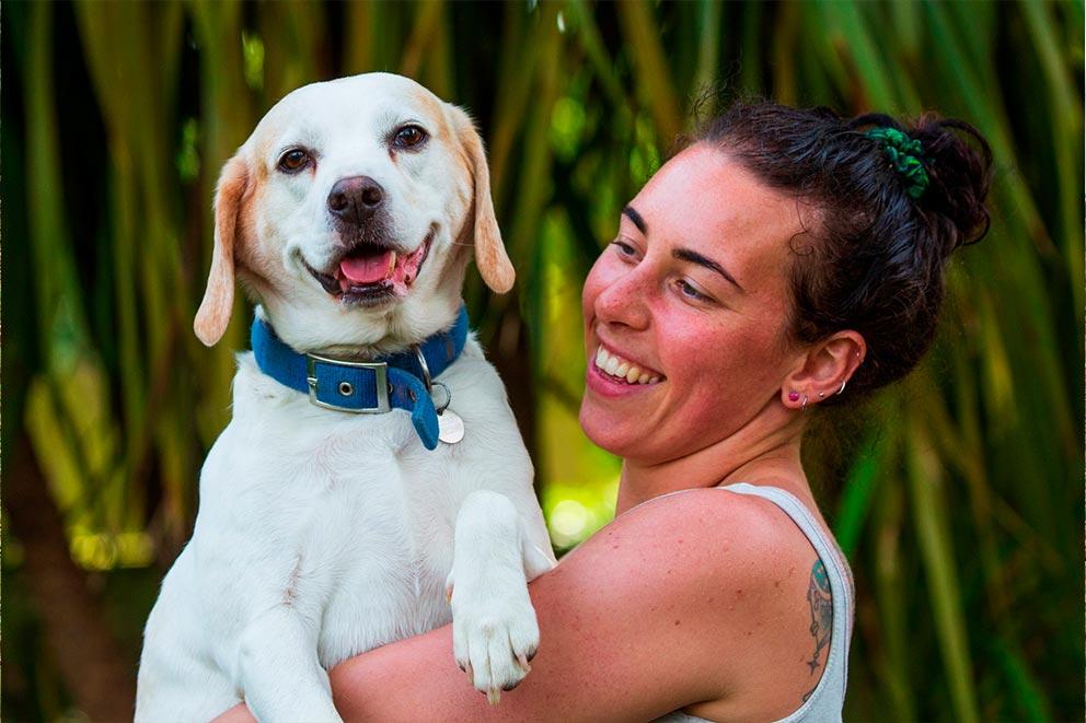 A lady holding a dog outdoors, smiling.