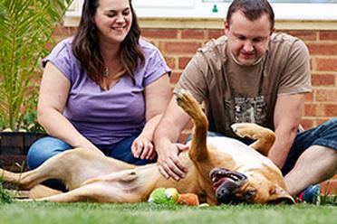 man and woman fussing a brown dog outside, they are both smiling