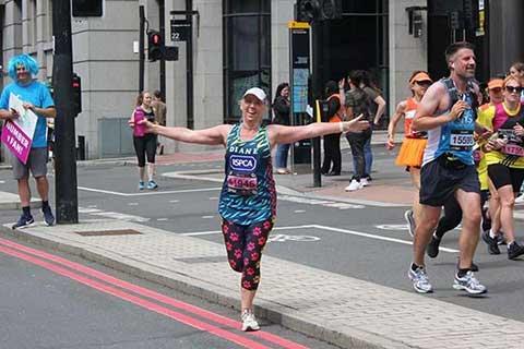 A woman running for the RSPCA wearing a Team Animal vest standing with arms outstretched.