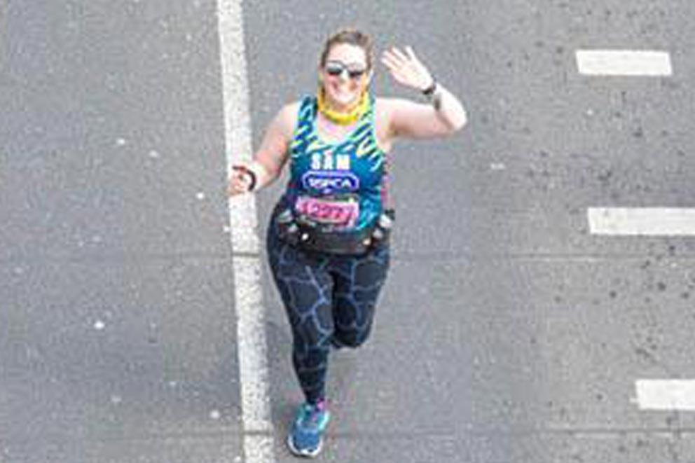 A charity runner waving to camera while running in the road as part of an organised running event.