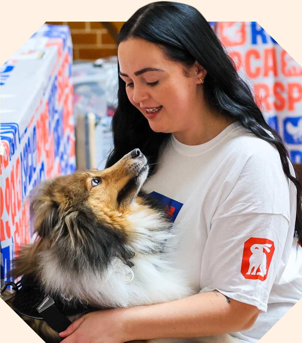 Awoman with dark hair looks fondly at a dog, she is smiling