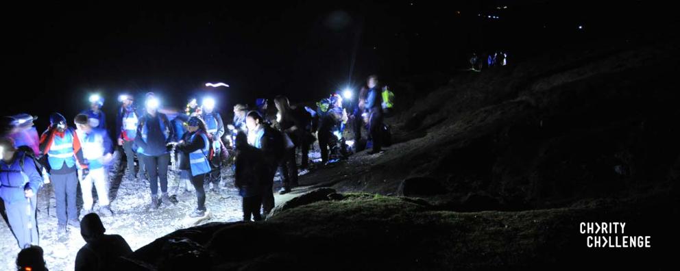 A large group of charity fundraisers walking at night wearing headtorches.